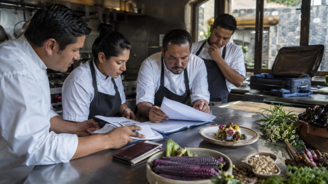 Chef y brigada mexiquense revisan documentos y un platillo listo para una convocatoria gastronómica internacional, escena documental mexicana.